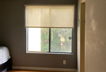 Partially open roller window shades in a bedroom, softly filtering sunlight and creating a relaxing atmosphere.