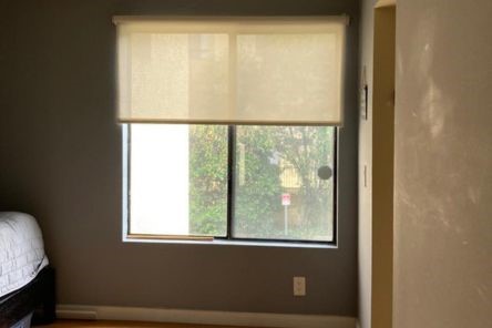 Partially open roller window shades in a bedroom, softly filtering sunlight and creating a relaxing atmosphere.